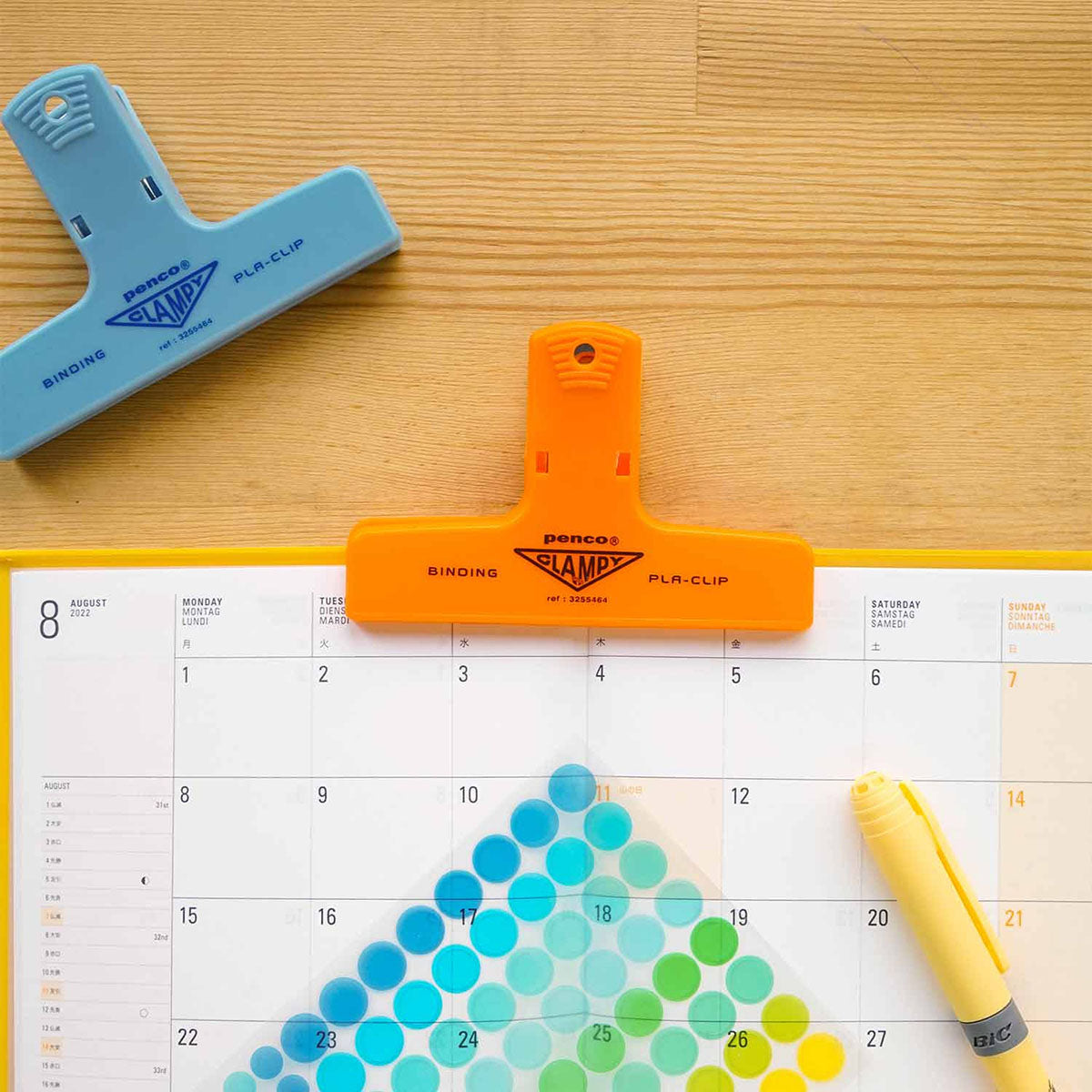 Plastikowe klipsy do papieru w kolorze niebieskim i pomarańczowym na biurku.