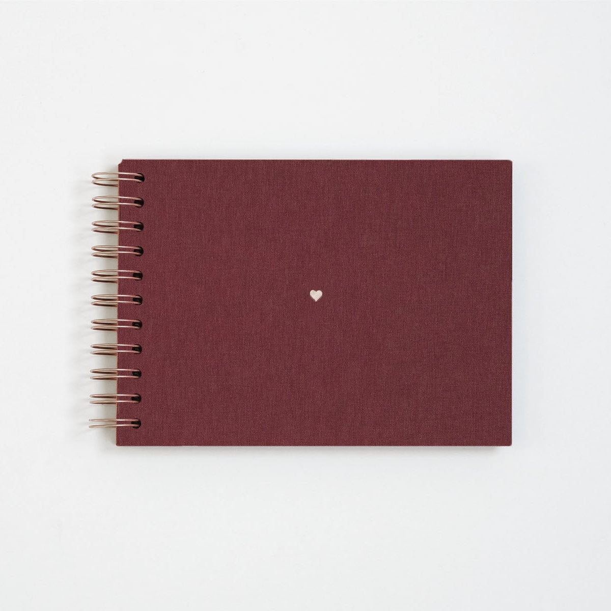 Płócienny album na zdjęcia w kolorze bordowym. Wykończony miedzianą spiralą oraz małym serduszkiem w centrum.